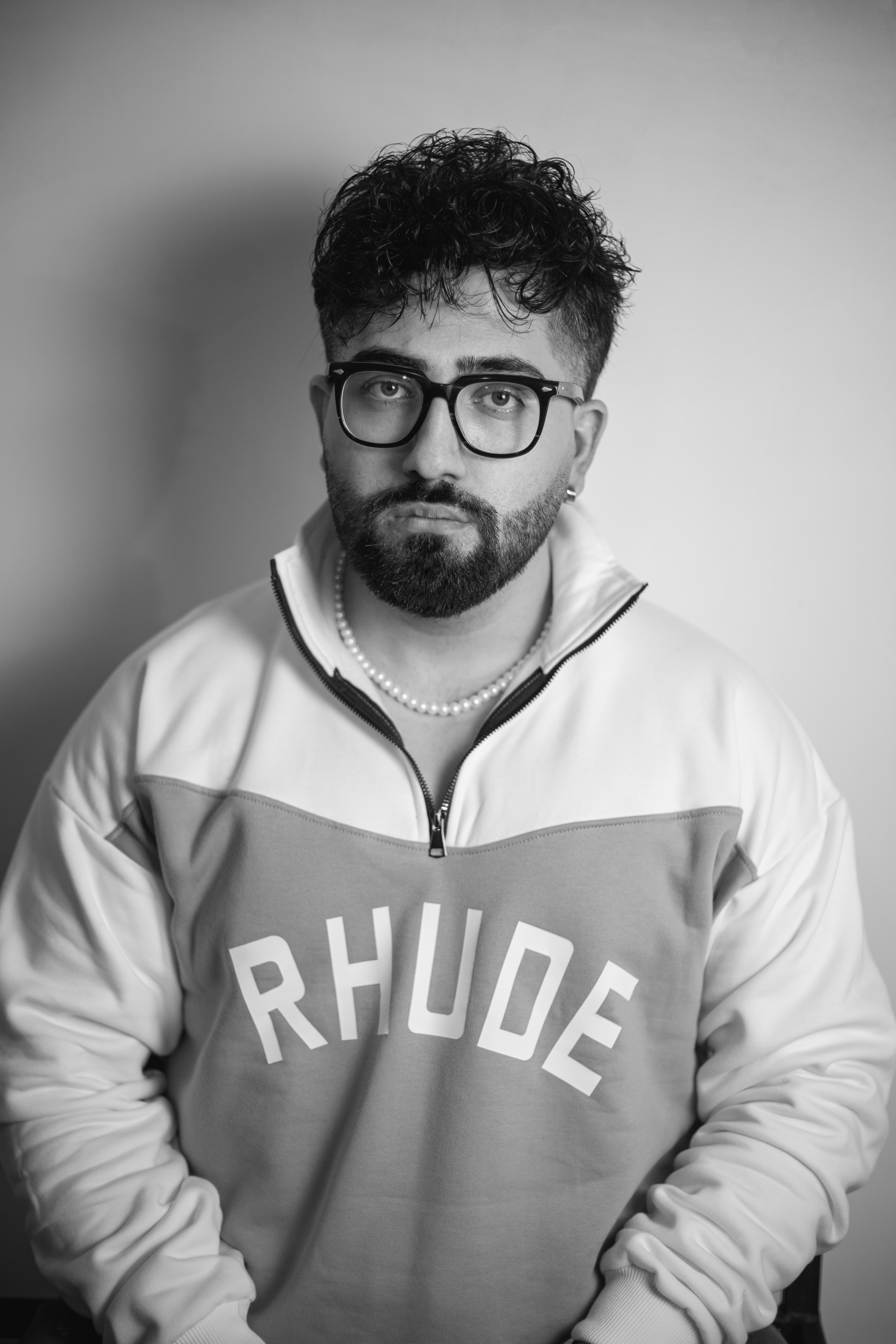 Studio portrait of a bearded man with glasses and a sweatshirt in black and white.