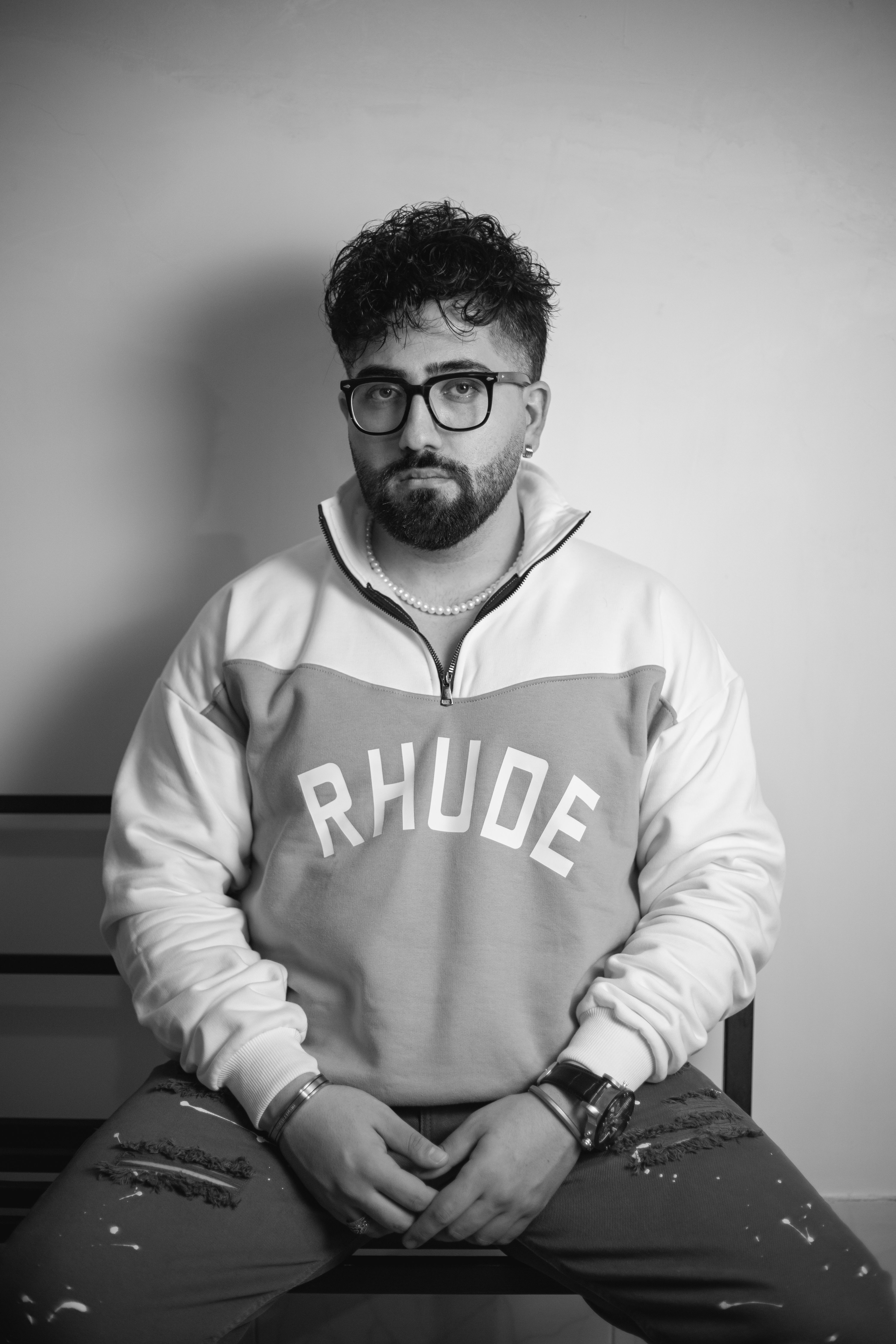 Black and white portrait of a man in glasses and stylish sweater, seated indoors.