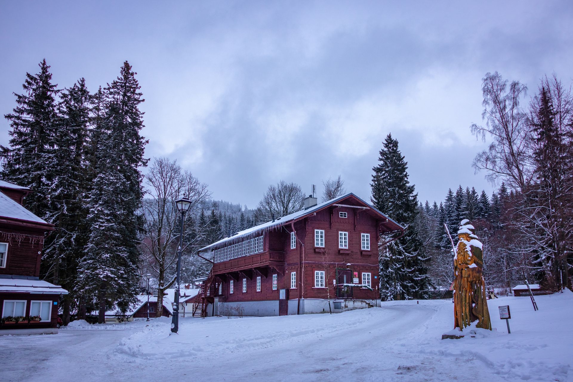 Rustic wooden chalet surrounded by snow and tall trees in winter landscape.