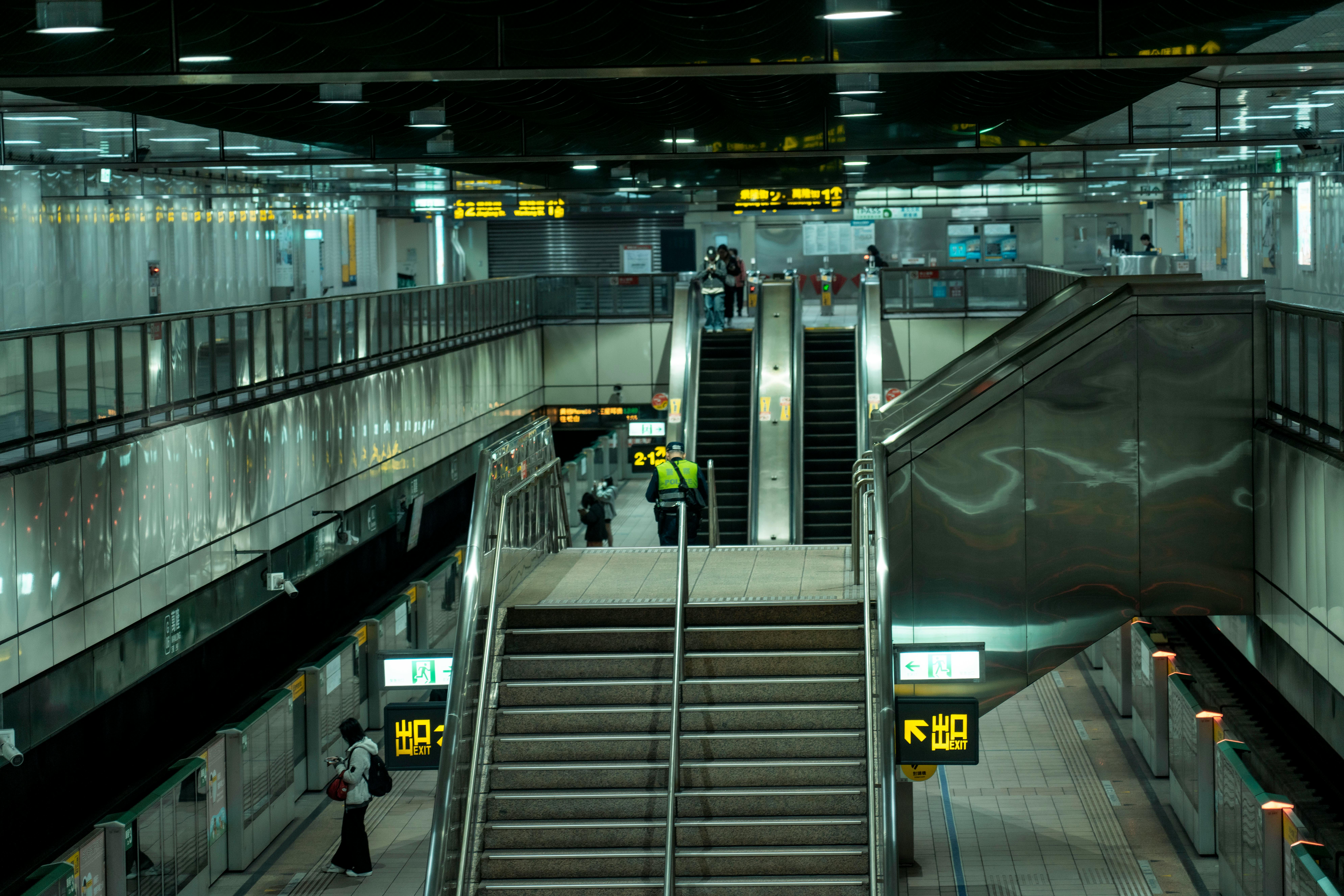 Busy Taipei metro station interior showing escalators and directional signs, capturing urban transit life