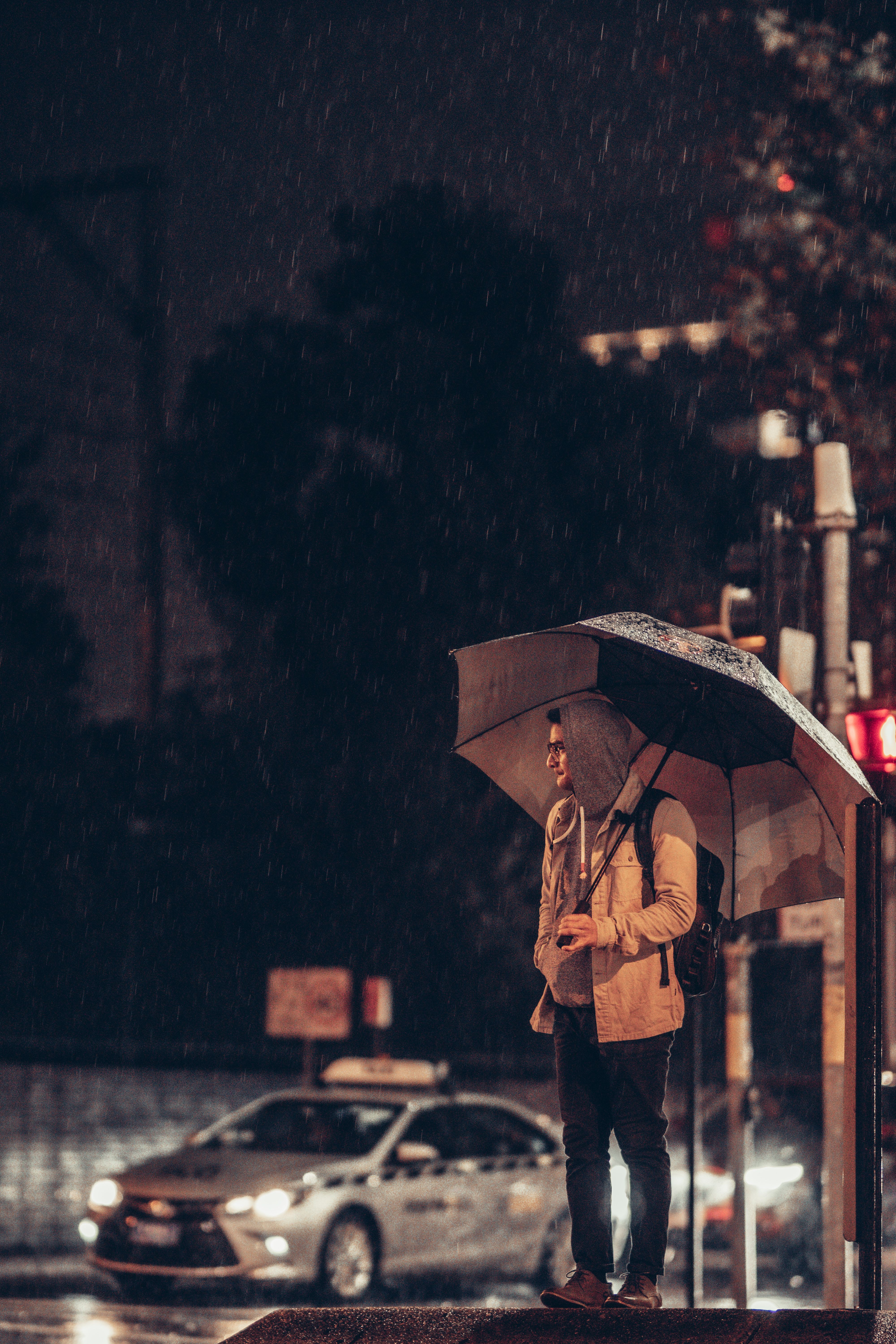 Person standing in rain with umbrella on busy city street at night.