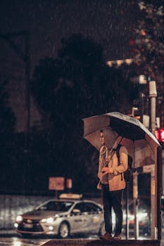 Person standing in rain with umbrella on busy city street at night.