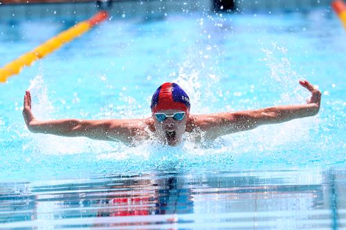 Free Swimmer performing butterfly stroke in competition pool on a sunny day. Stock Photo