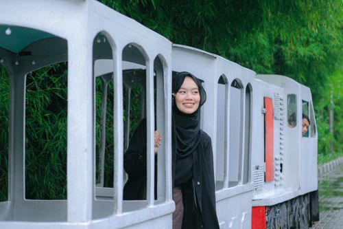 Free A young woman smiles while riding a charming miniature train in lush green surroundings. Stock Photo