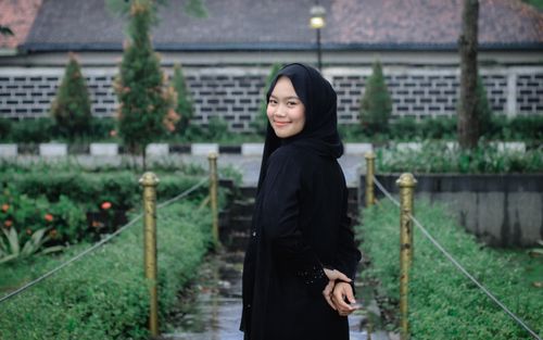 Free A young woman in a hijab smiles in a beautiful outdoor garden setting with lush greenery. Stock Photo