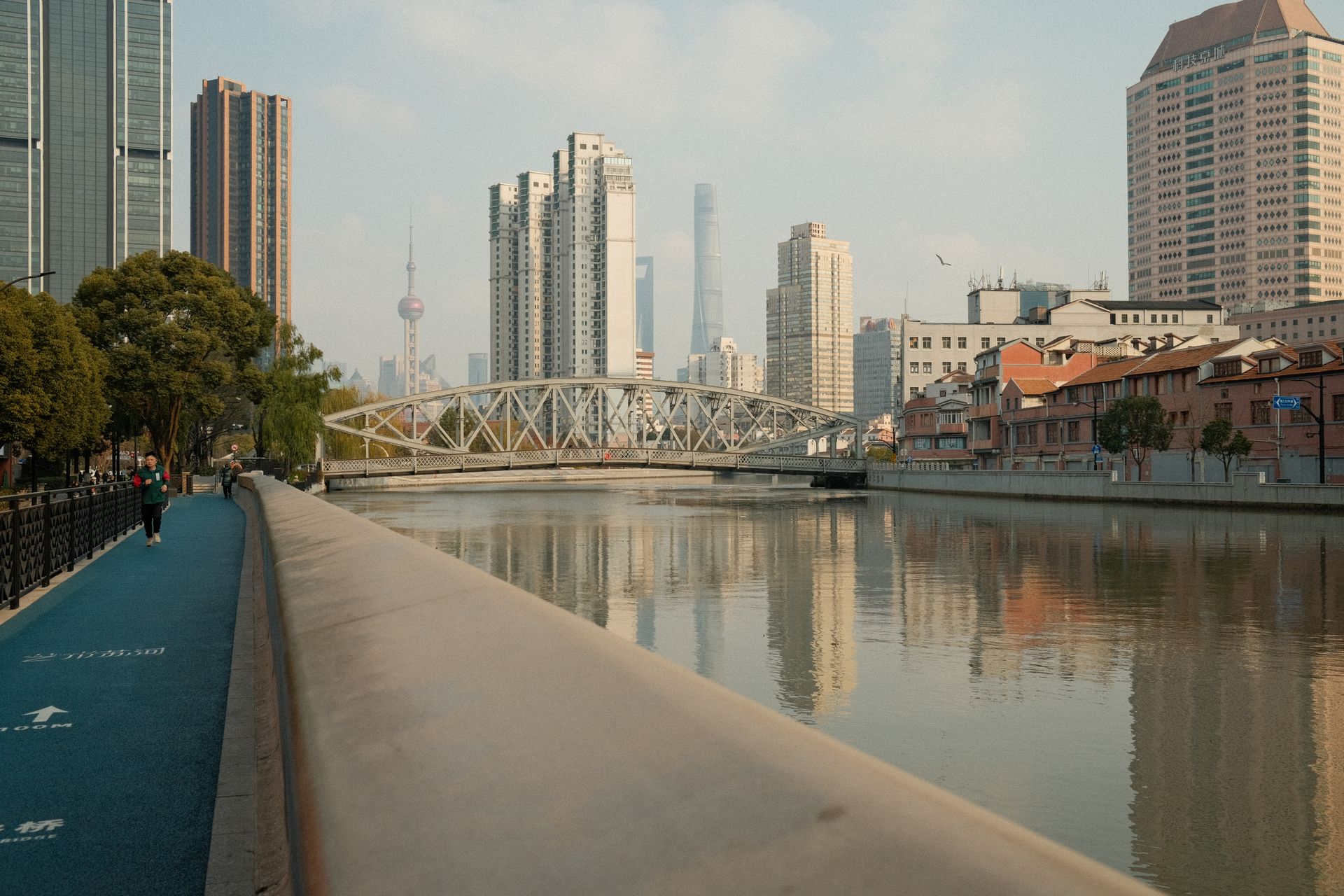A quiet day along a Shanghai canal with the city skyline and iconic bridge.