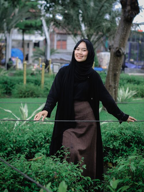Free Woman wearing a black hijab and coat, smiling in a lush green park setting outdoors. Stock Photo