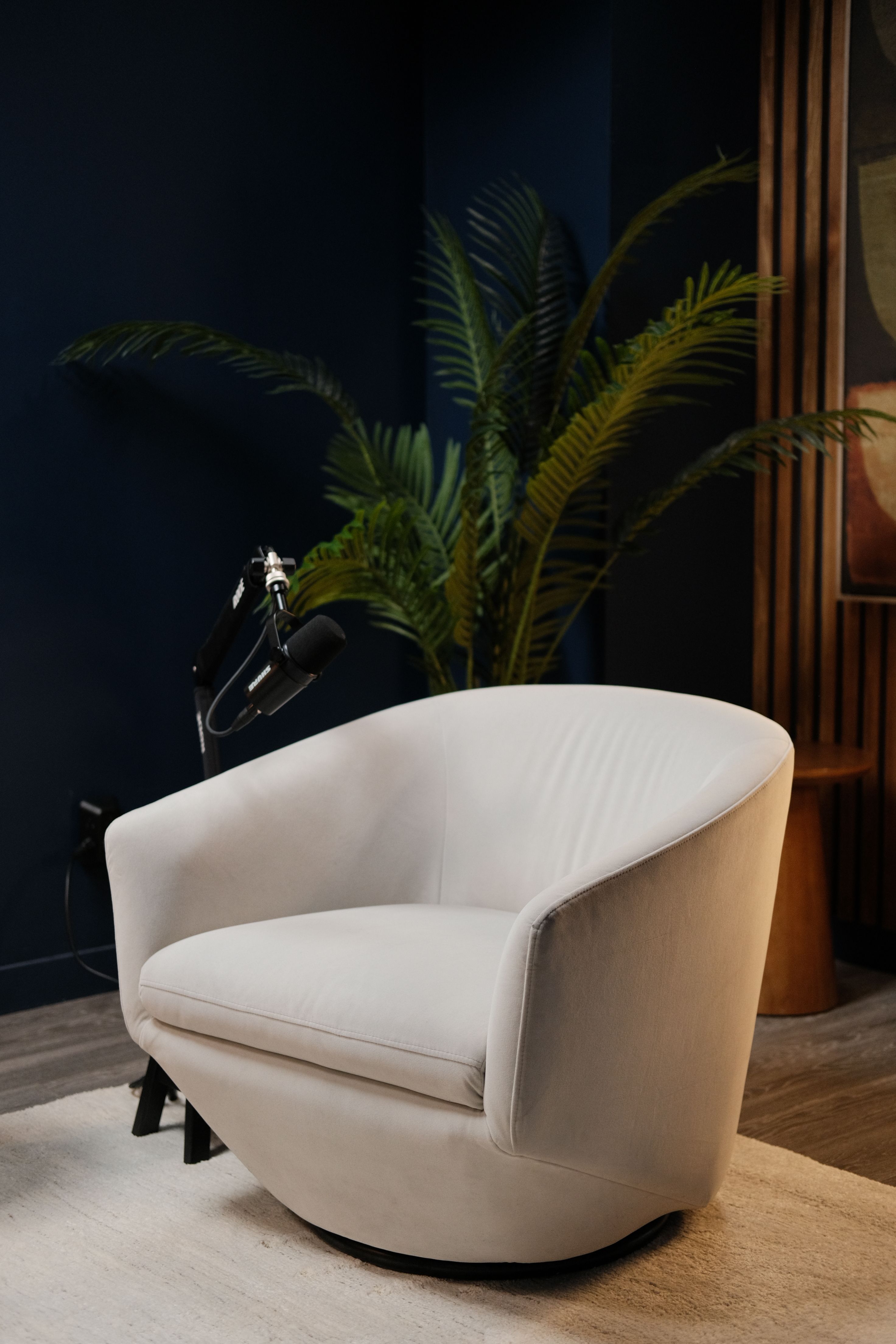 A white armchair and microphone beside wood slat panelling on a navy podcast set