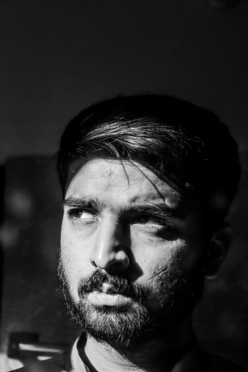 Free A dramatic black and white portrait of a man contemplating, casting deep shadows. Stock Photo