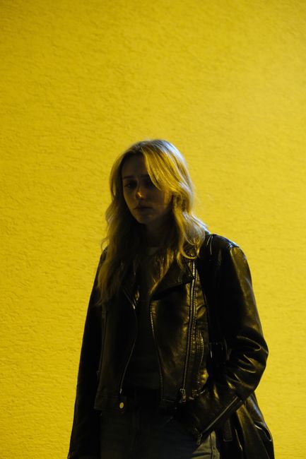 Mysterious woman in leather jacket against vibrant yellow background at night.
