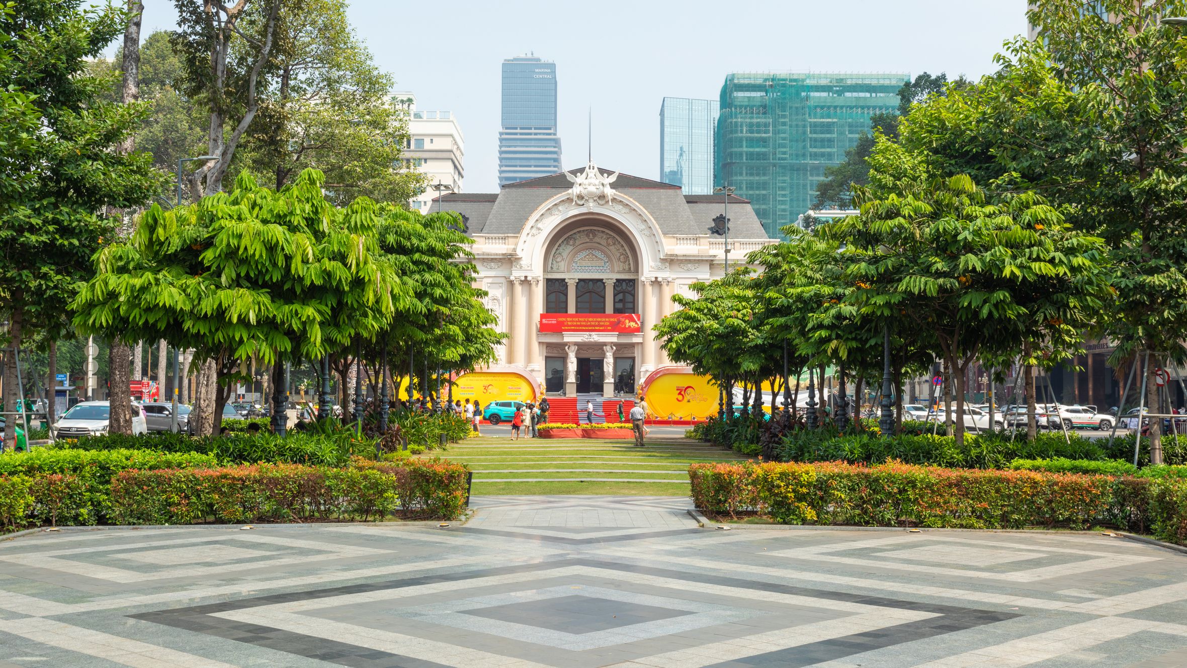 Scenic view of the vibrant Ho Chi Minh City Opera House, framed by lush green trees, during the day.
