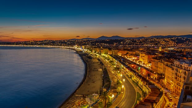 Beautiful twilight view of Nice city and coastline in France, showcasing illuminated streets and scenic bay. by Pierre Blaché