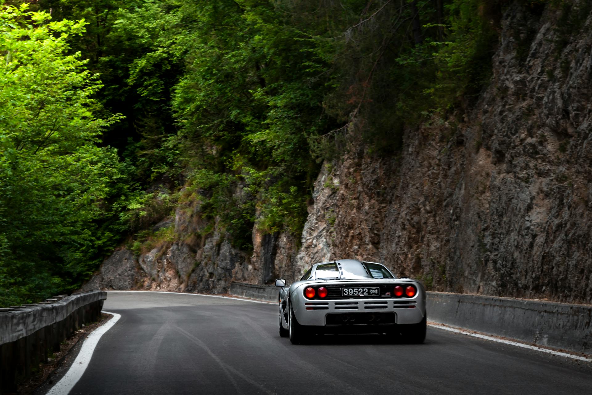 A sleek supercar navigating a winding mountain road surrounded by lush greenery.