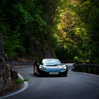 A sleek supercar effortlessly navigates a winding mountain road surrounded by lush greenery.