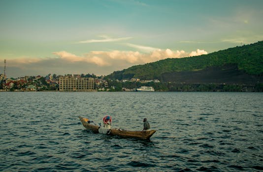 Fishermen in a wooden canoe on Lake Kivu against the backdrop of Goma cityscape and lush hills.
