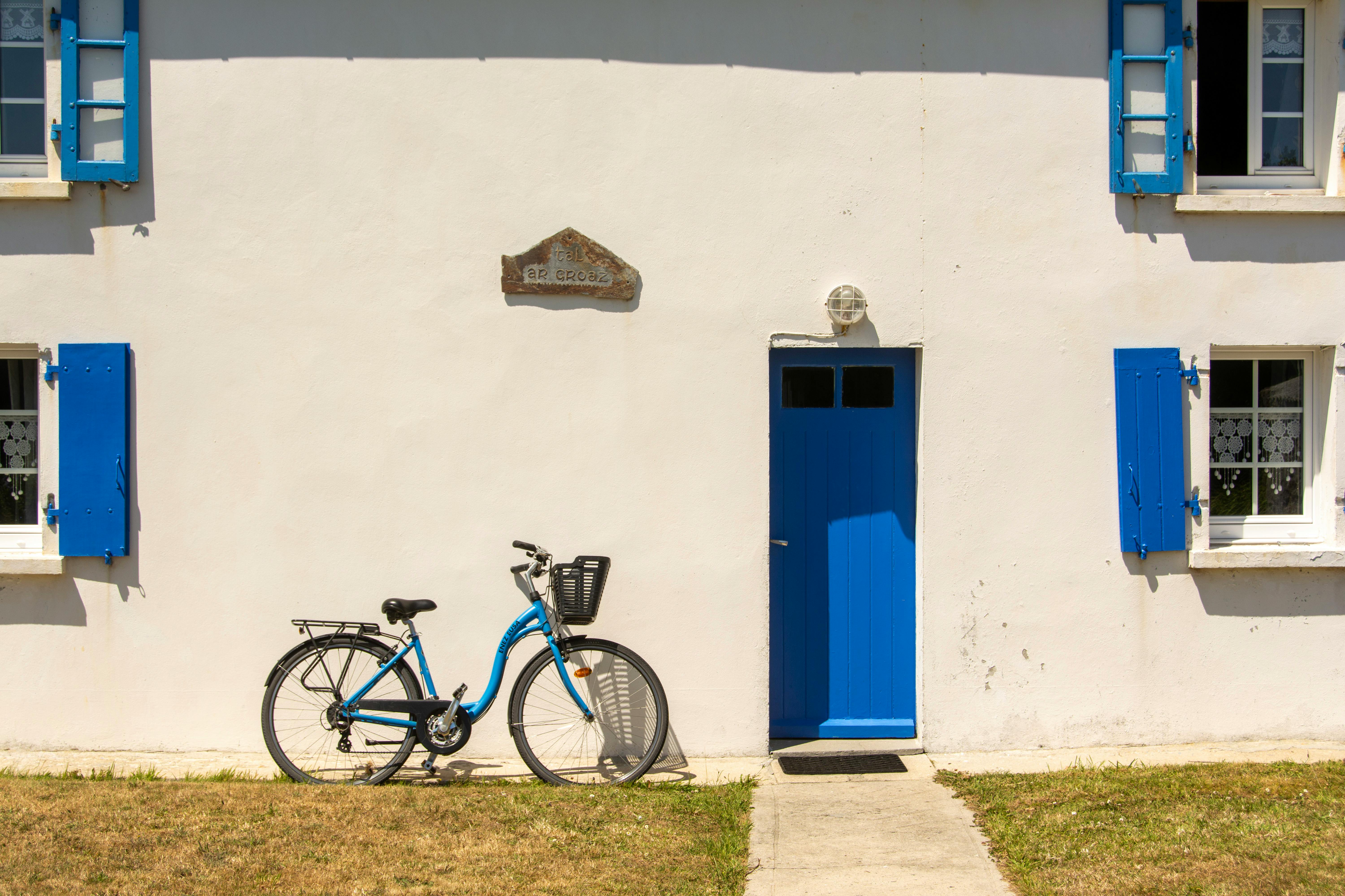A picturesque scene of a blue bicycle leaning against a white house with blue doors and shutters on a sunny day.