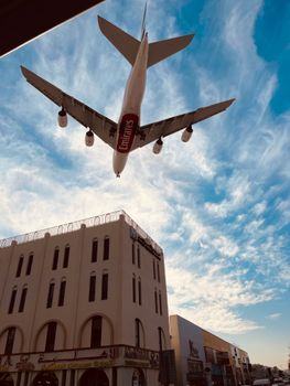 A large Emirates airplane soars over a Dubai neighborhood under a vibrant blue sky.