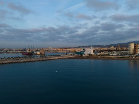 Stunning aerial view of Málaga harbor at sunrise with city skyline and mountains in the background.