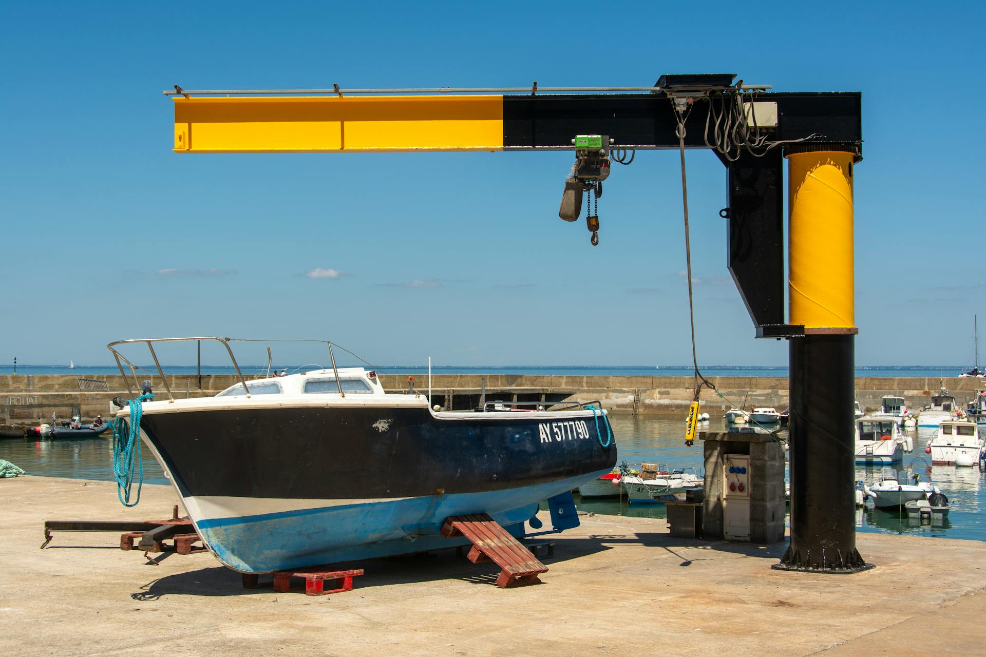 Powerful industrial crane lifting a boat in a marina under a clear blue sky.