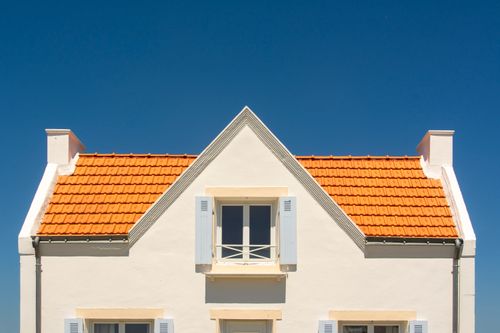 Free Front view of a house with orange tile roof and blue sky background. Stock Photo