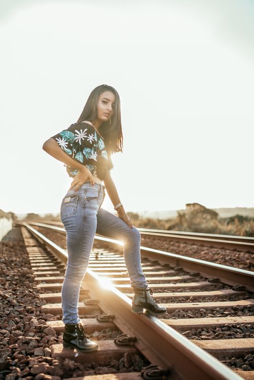 Free Confident young woman posing on sun-drenched railway tracks, showcasing fashion and style. Stock Photo