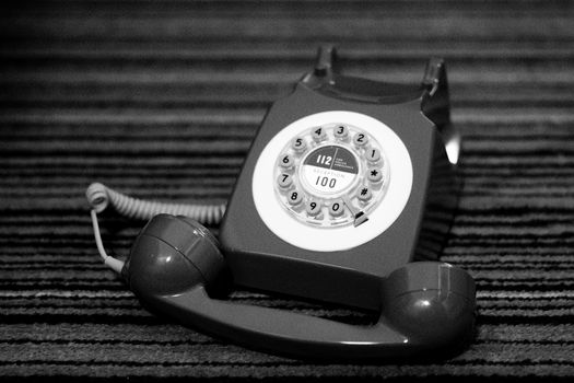 Black and white image of a classic rotary dial telephone resting on a striped surface.