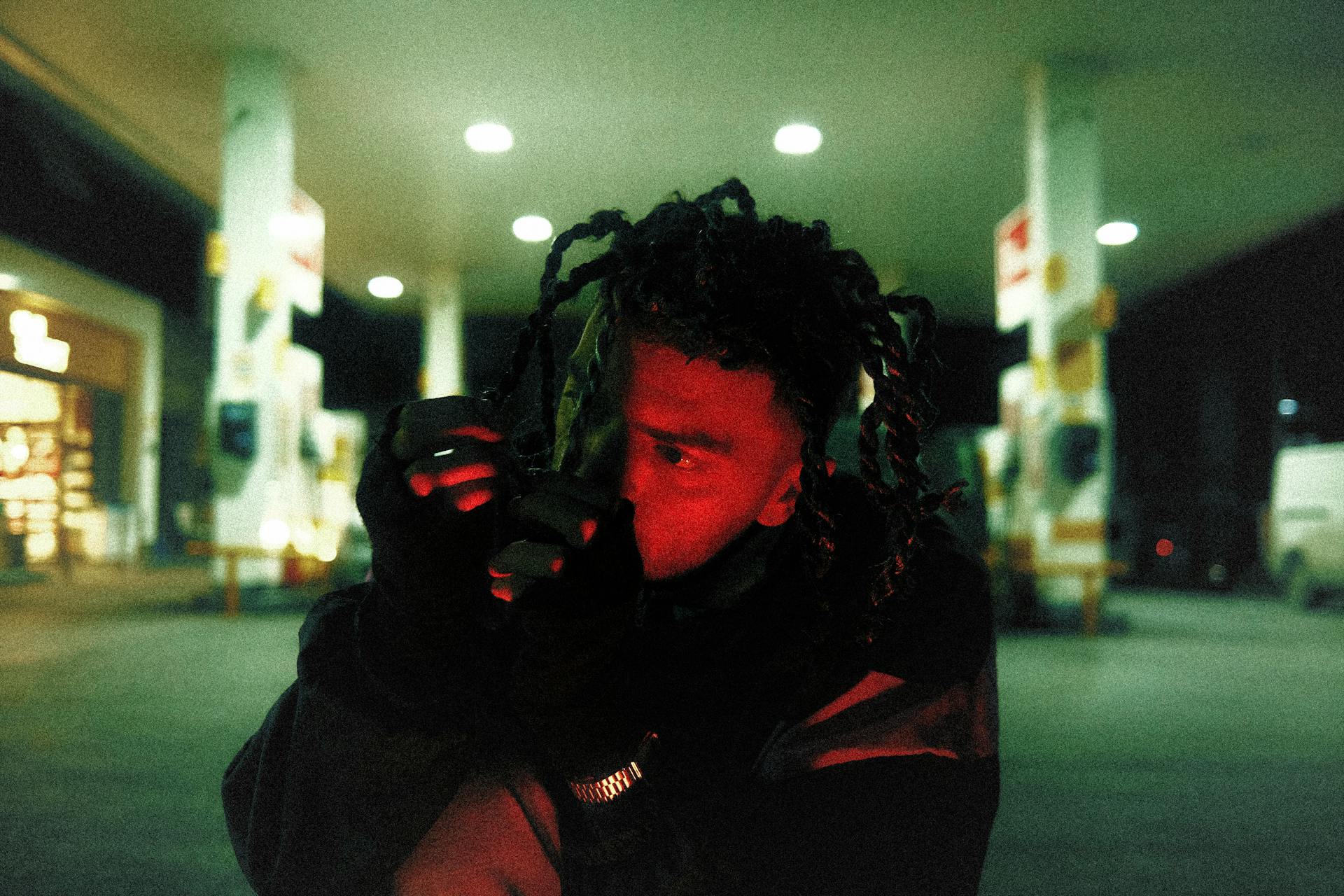 Portrait of a person at a gas station illuminated by vibrant red light at night.