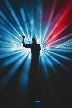 Dramatic silhouette of a performer on stage with vibrant blue and red lighting.