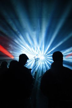 Silhouetted people enjoy a colorful light show at a live concert, creating a lively ambiance.