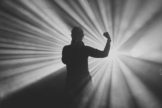 Black and white silhouette of a performer on stage with dramatic light rays.