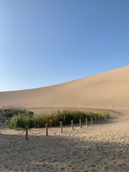 A tranquil oasis surrounded by vast sand dunes under a clear blue sky.