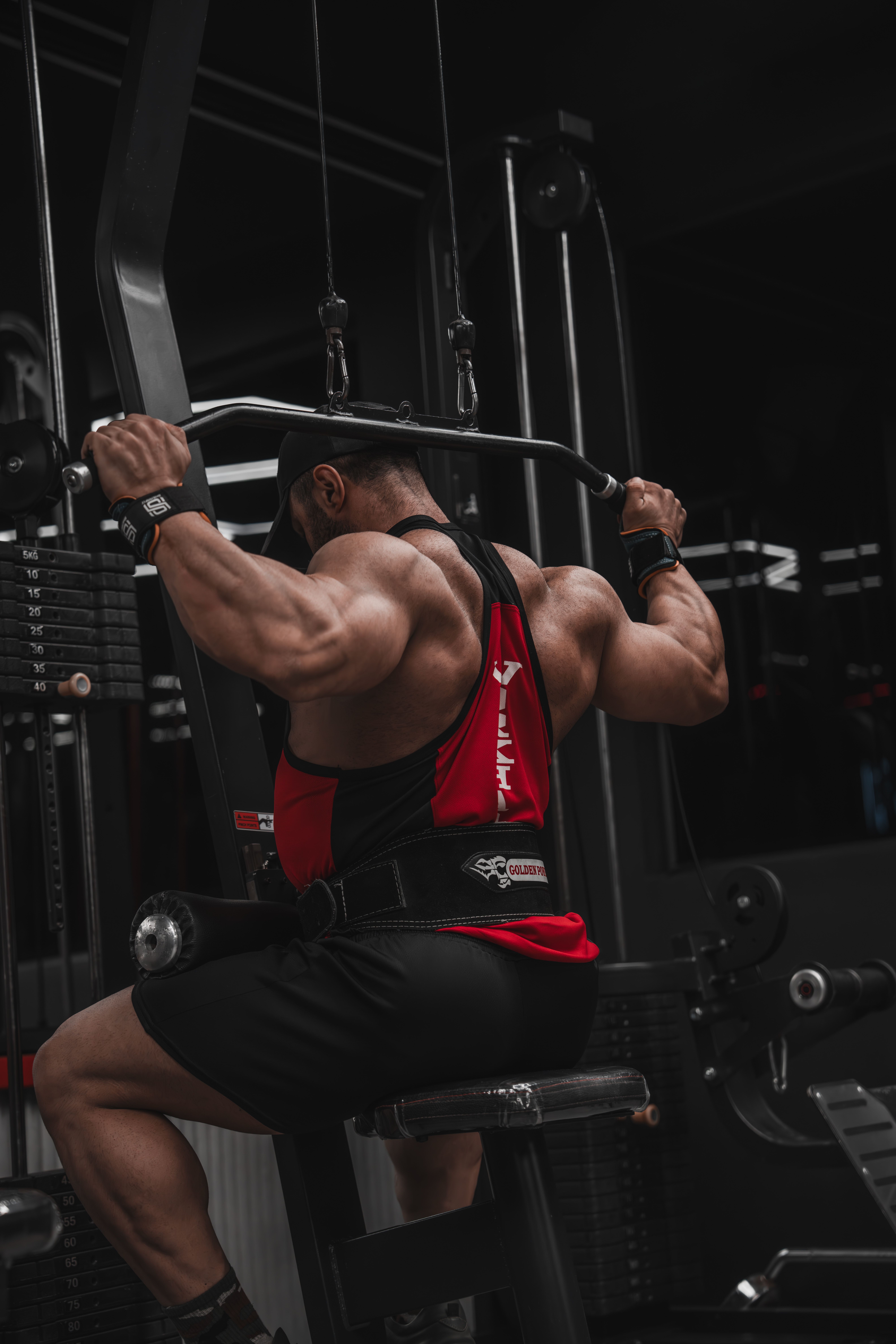 A muscular man doing lat pulldown exercise on a gym machine.