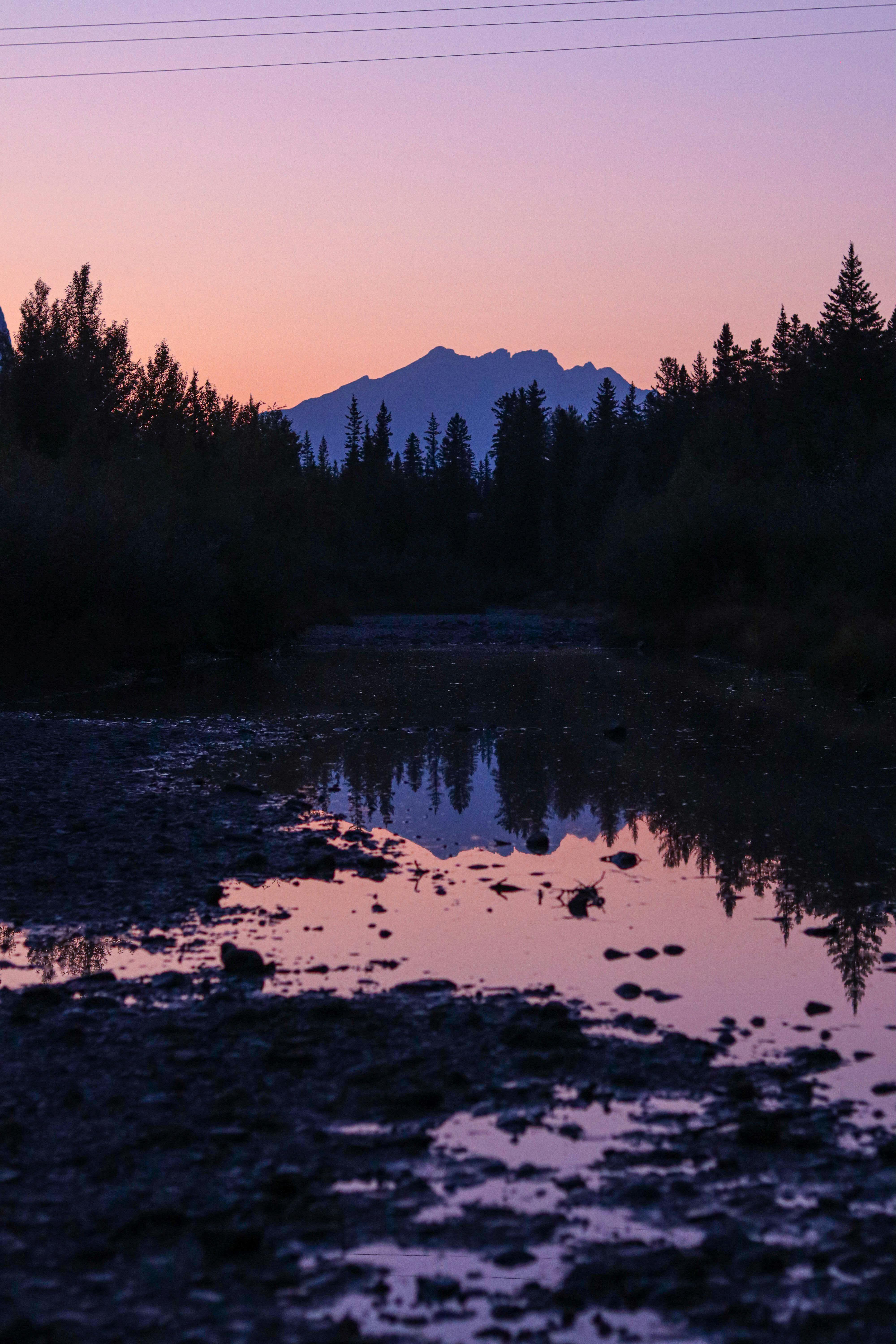 Mountain silhouette reflected in tranquil river with pink and purple dusk sky.