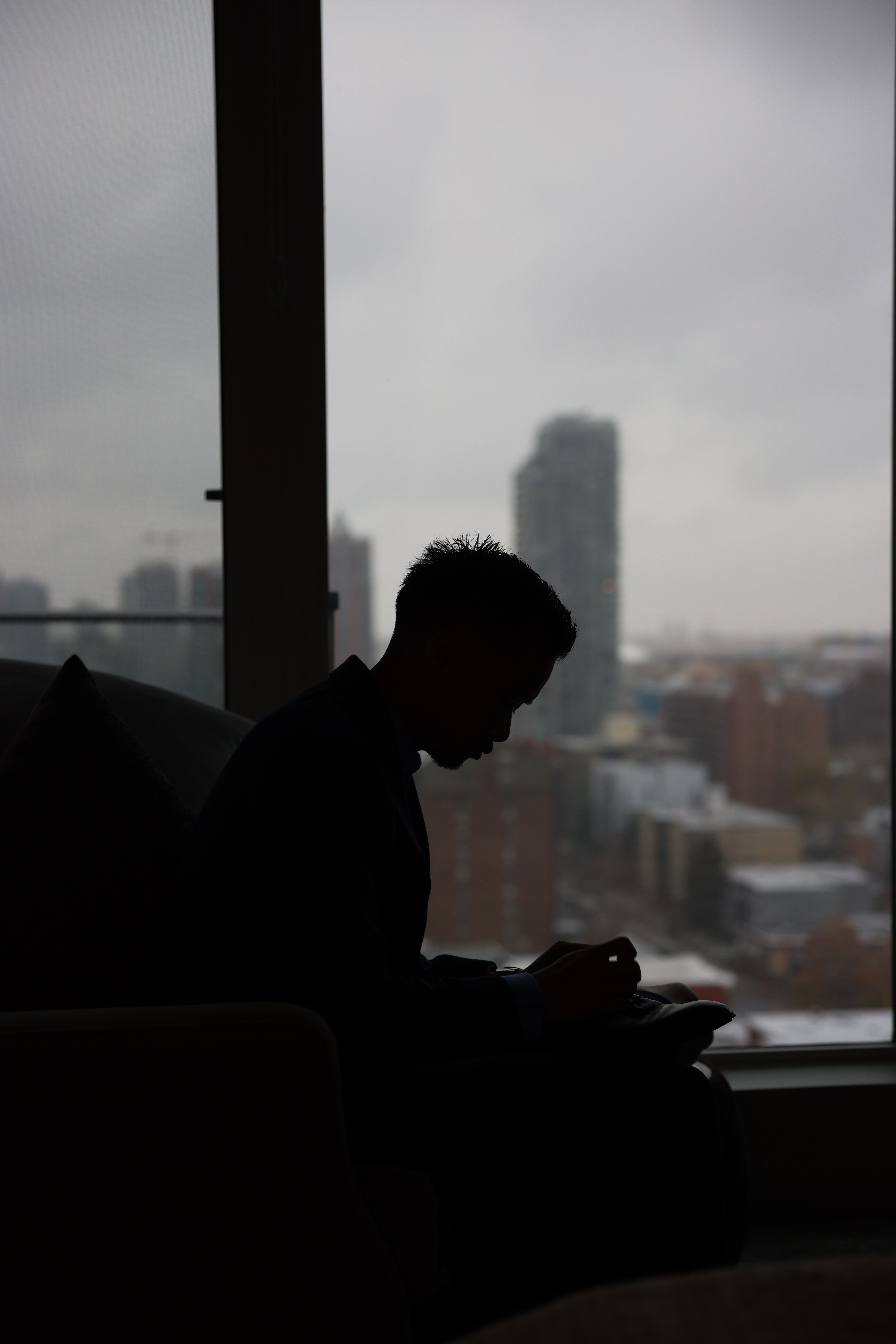 Silhouette of an adult by a window overlooking a cityscape on a cloudy day.