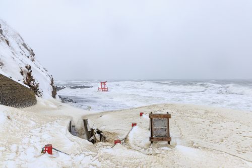 Free Winter scene of snow-covered beach and iconic red Torii gate in Shosambetsu, Hokkaido, Japan. Stock Photo