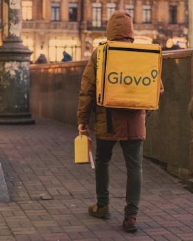 A person carrying a yellow delivery bag walking in a winter city street scene.