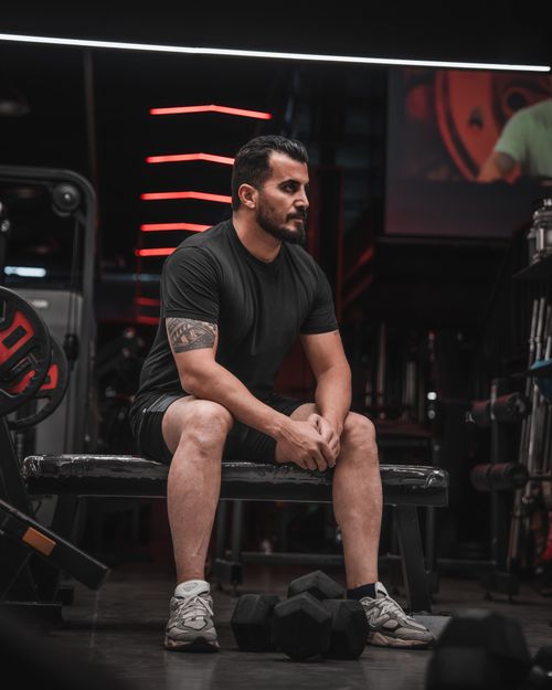 Free A man sits on a bench in a gym, taking a break from weightlifting, surrounded by equipment. Stock Photo