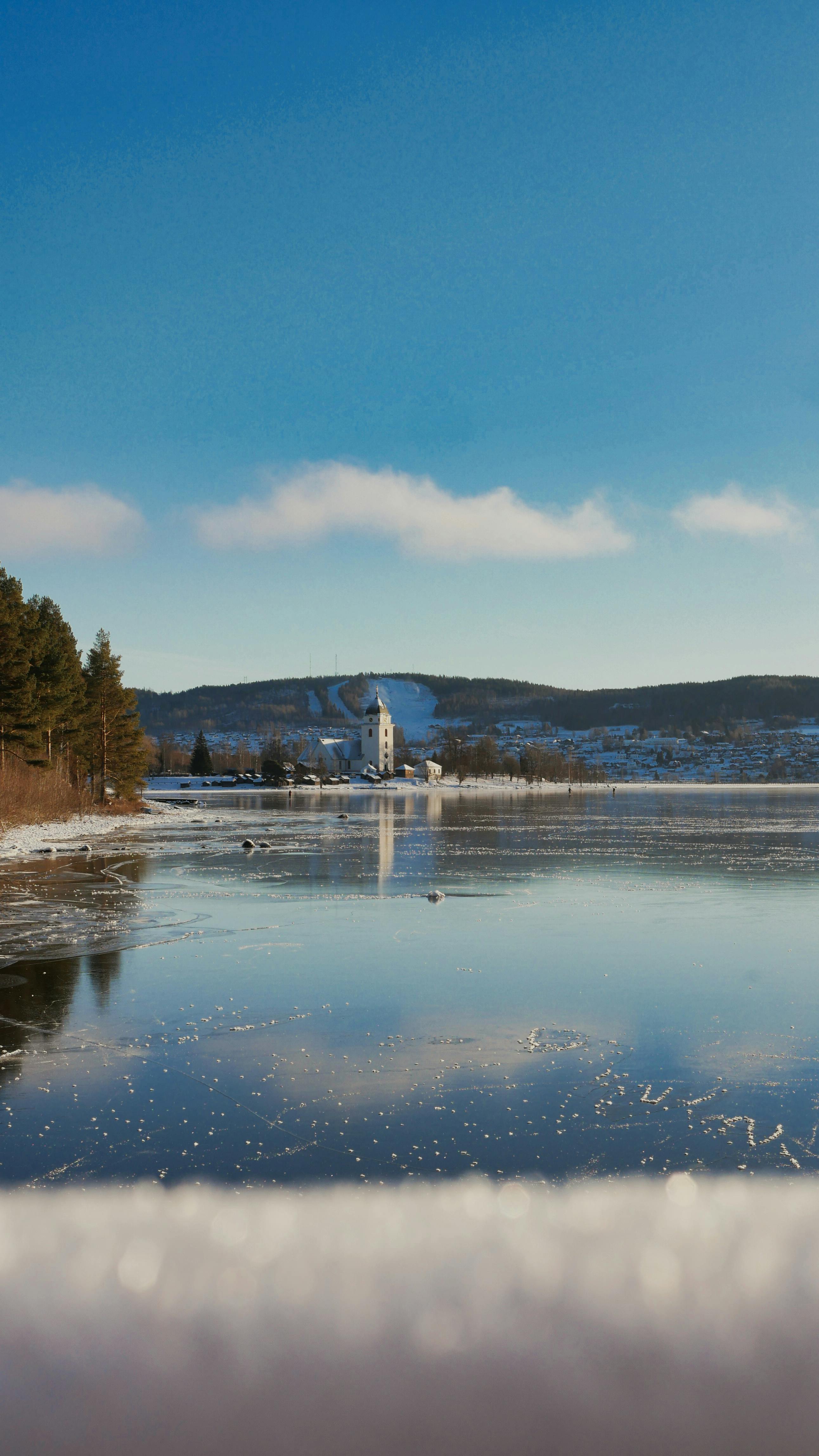 Tranquil winter landscape of a frozen lake in Rättvik, Sweden, with distant hills and a church.