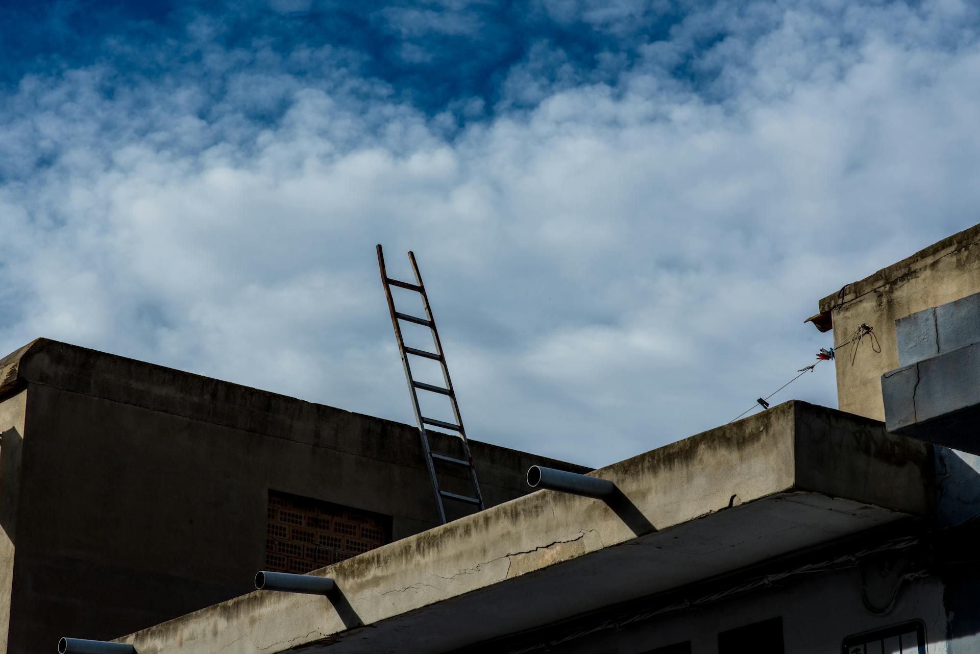 A ladder resting against a rooftop under a bright blue sky with scattered clouds.