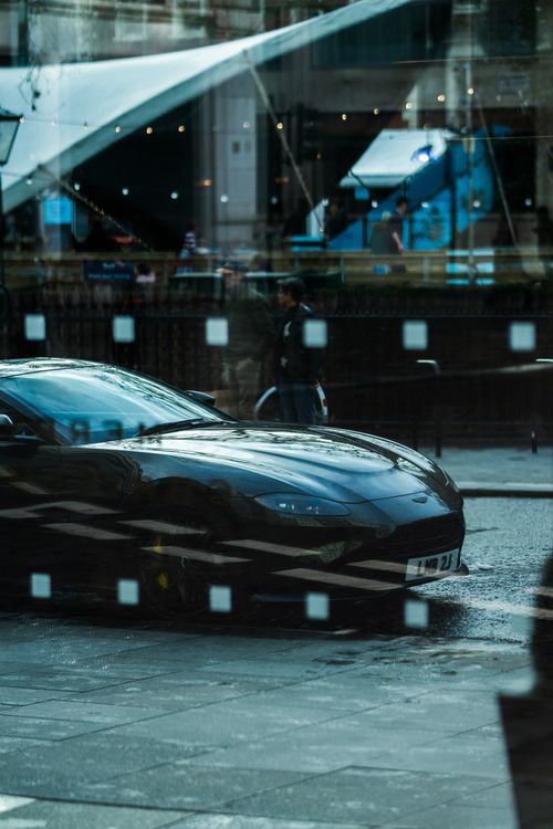 Free A black sports car displayed with an artistic reflection through glass in a bustling city environment. Stock Photo