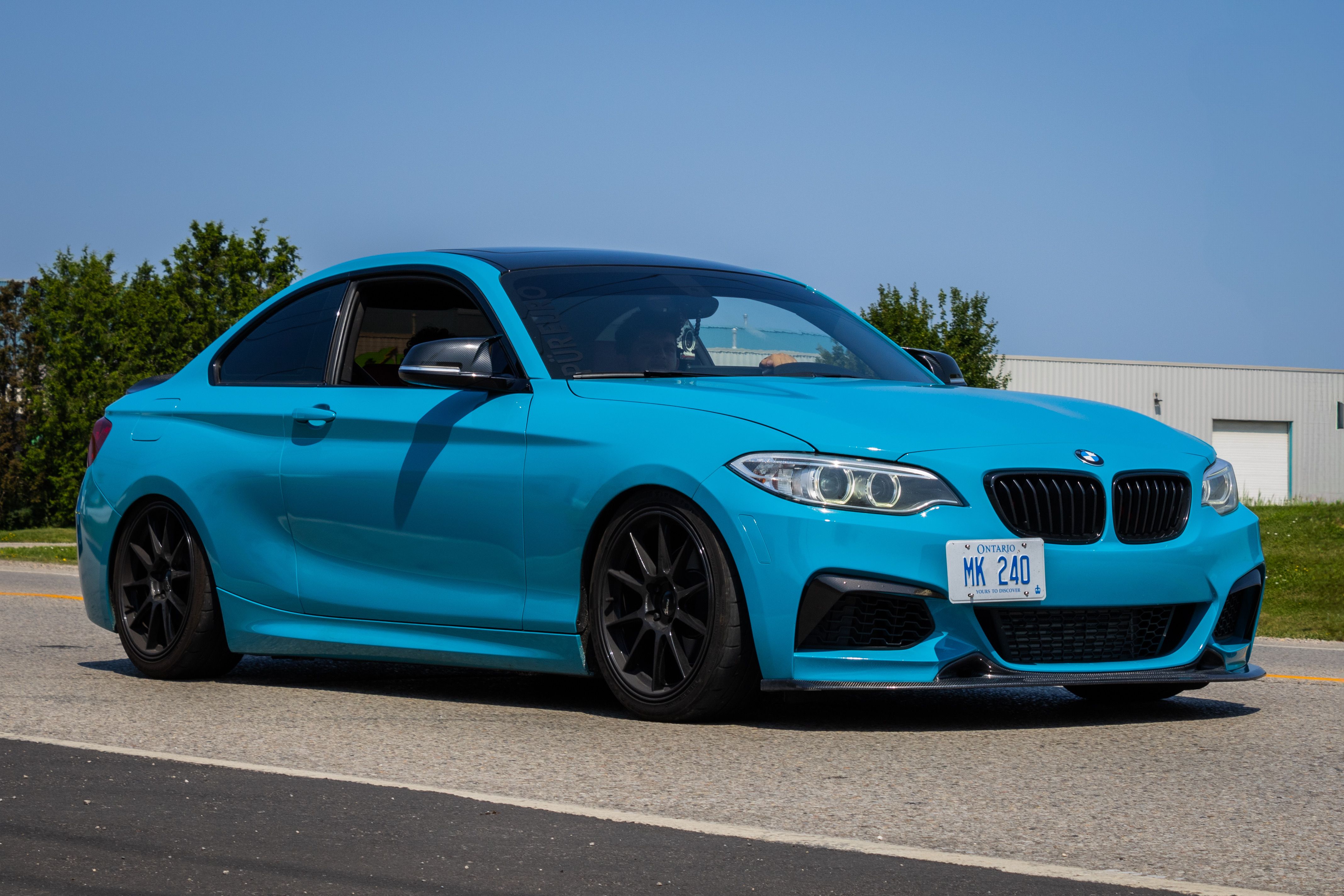 A sleek blue sports car parked on the road under a bright blue sky.