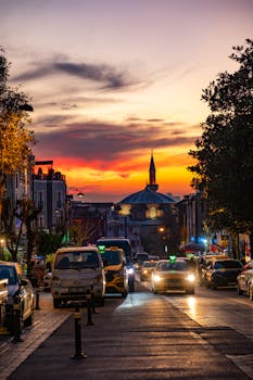 A vibrant city street bustling with cars at sunset, featuring a mosque silhouette against a dramatic sky.