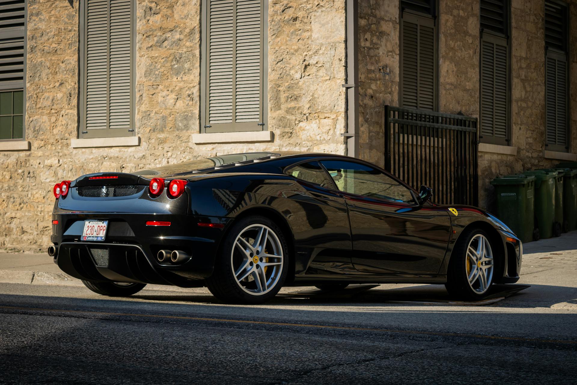 Black luxury sports car parked beside a rustic stone building in urban setting.