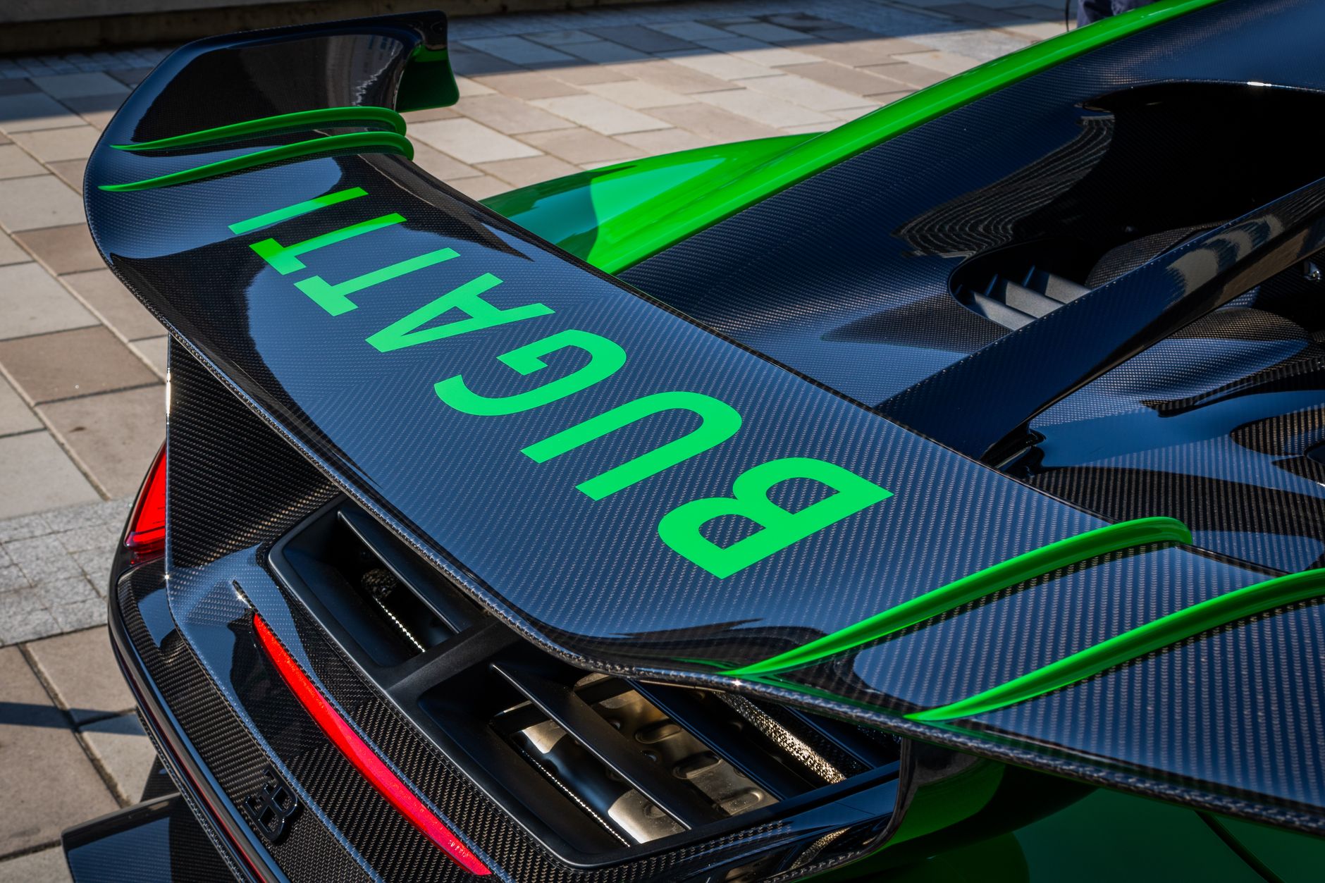 Detailed image of a carbon fiber car spoiler with a visible logo in an urban setting.