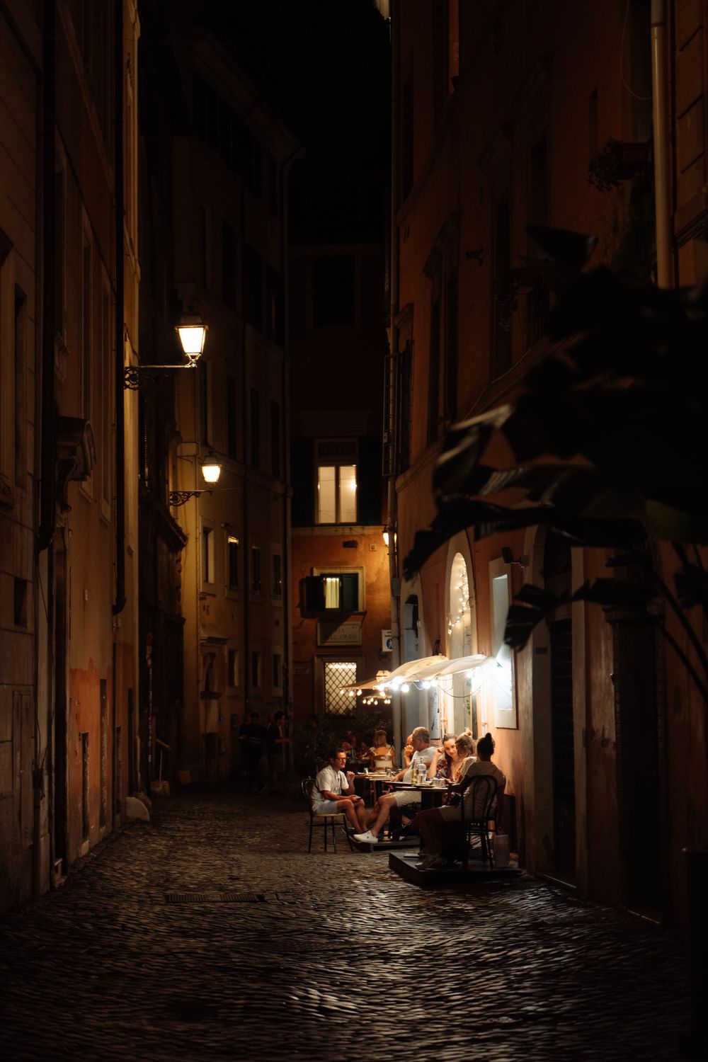 Cena íntima en una callejuela romana al anochecer, iluminada por farolas