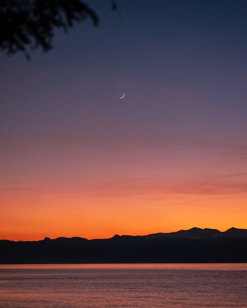 Free A tranquil sunset scene with a crescent moon above calm waters, perfect for peaceful themes. Stock Photo