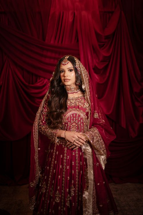 Free A bride in traditional red attire with intricate gold embroidery stands gracefully. Stock Photo