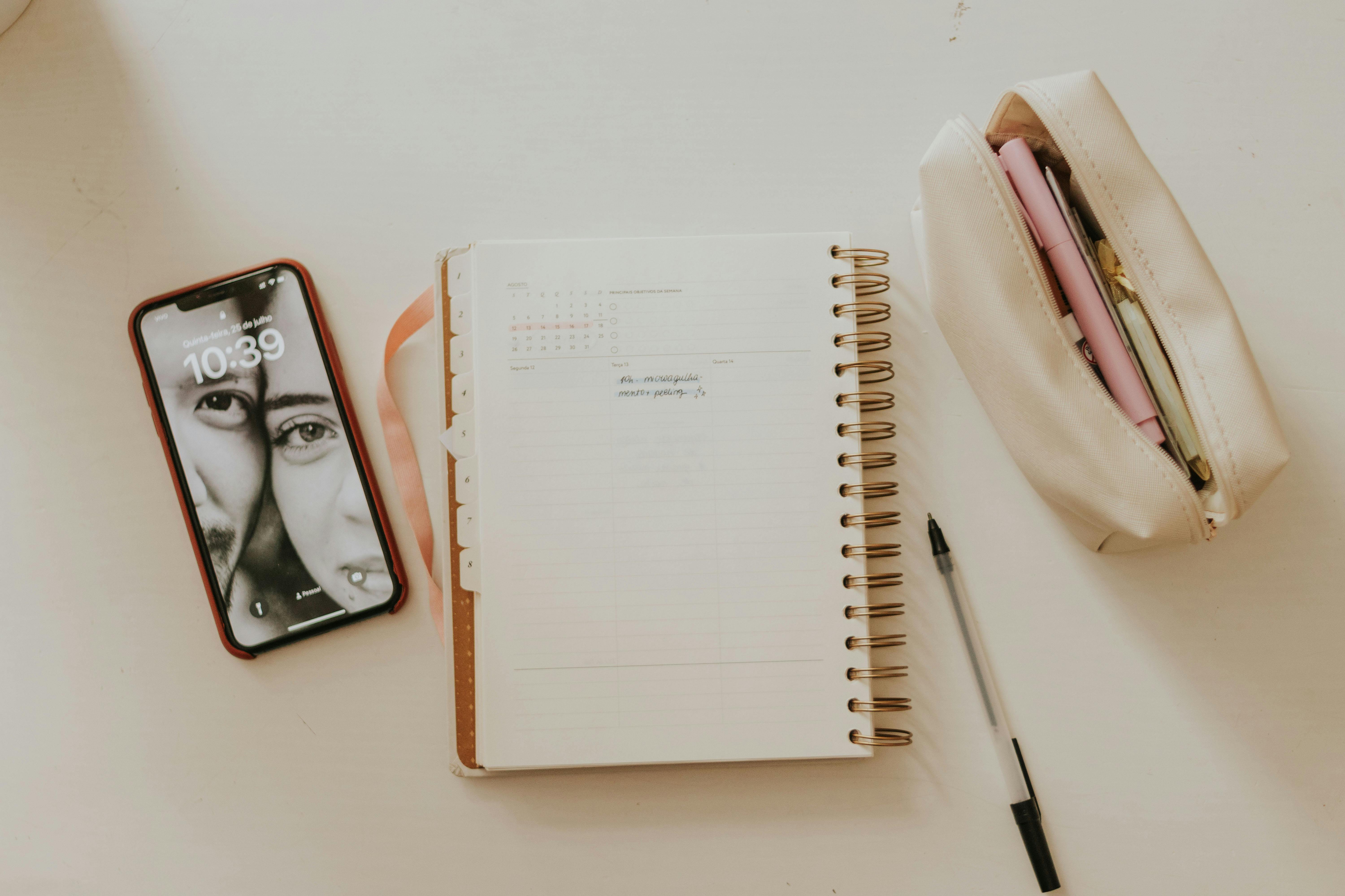 A neat workspace featuring a smartphone, open planner, and stationery items on a desk.