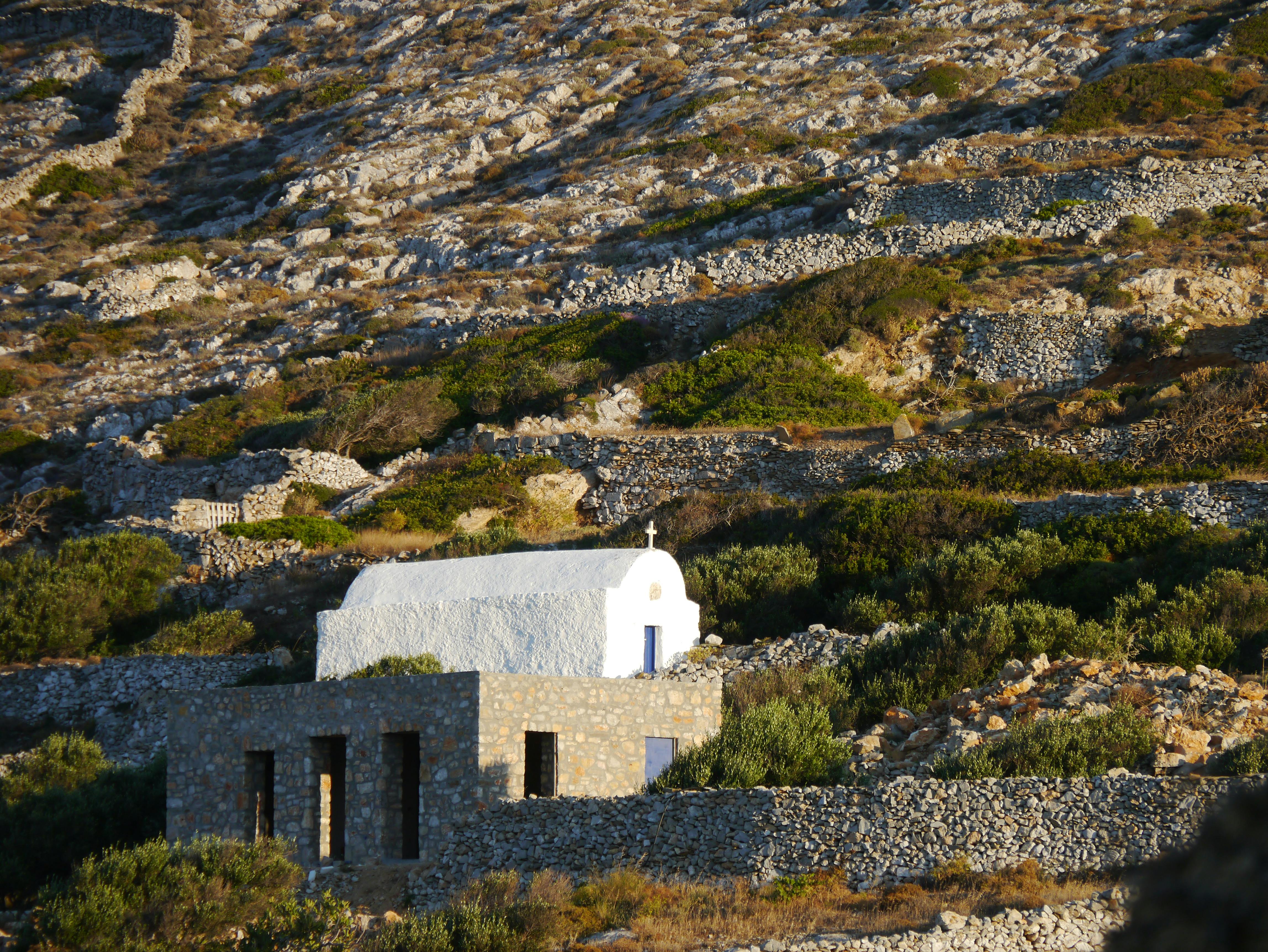 A picturesque white chapel nestled amidst rugged terrain with stone terraces.
