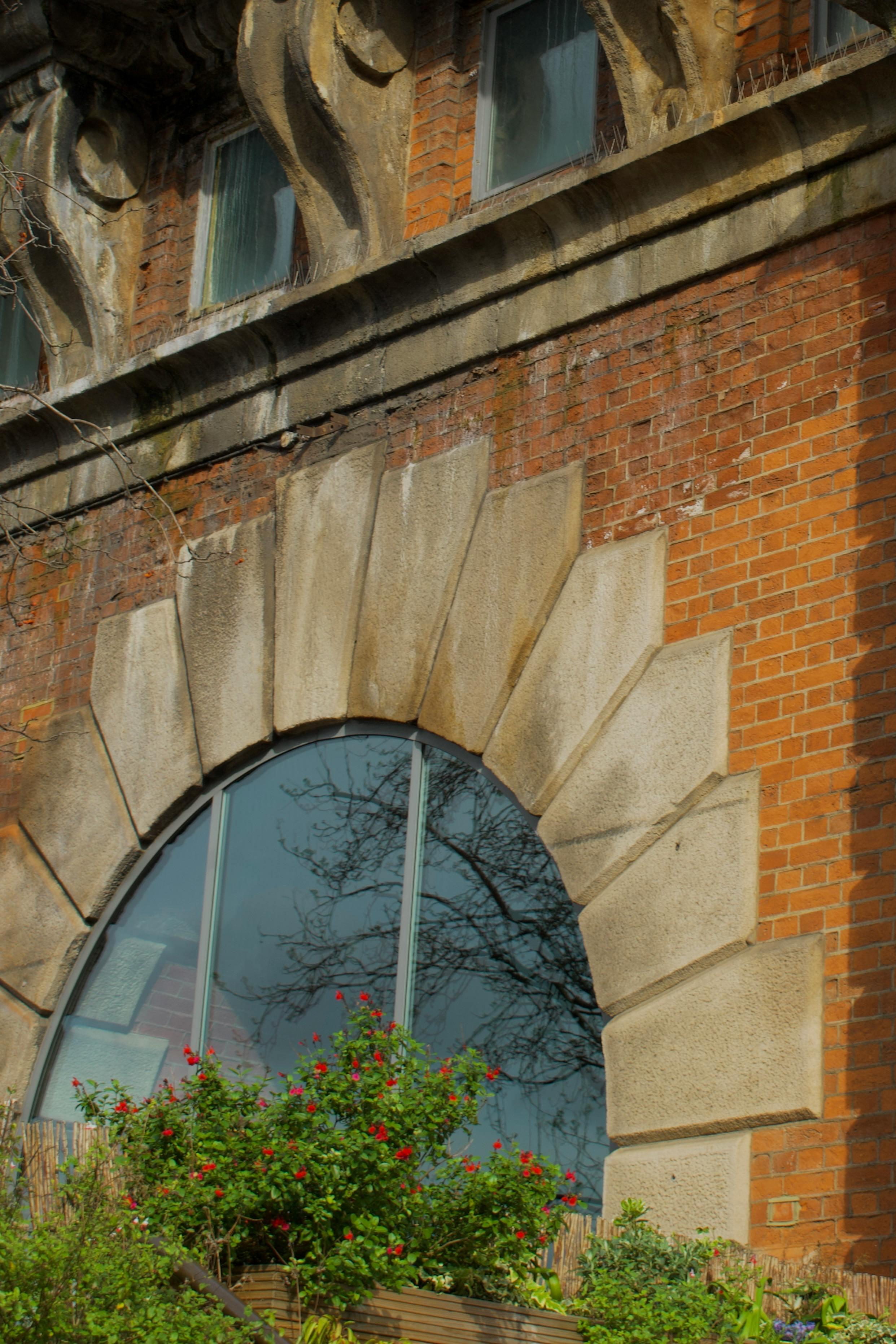 Close-up of a historic brick building featuring an arched window and green plants.